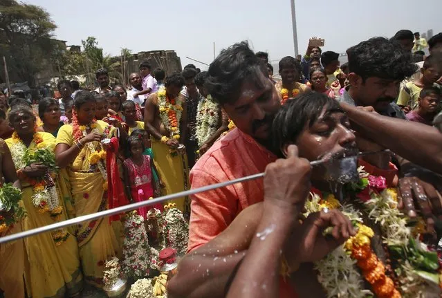 A devotee gets his mouth pierced with a trident as others watch during a religious procession dedicated to Goddess Mariamman in Mumbai, India, April 19, 2016. (Photo by Danish Siddiqui/Reuters)
