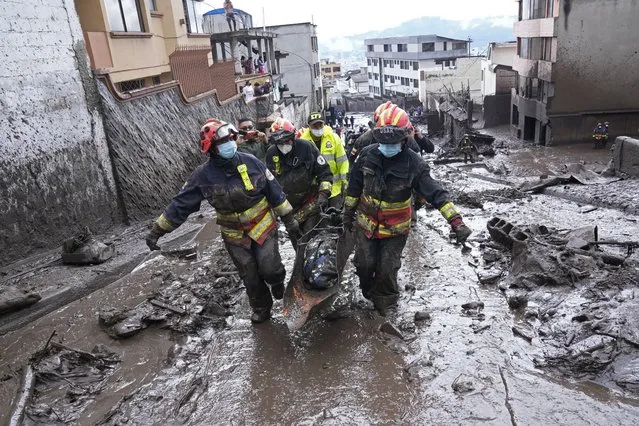 Rescue workers carry away the body of a victim after flash flooding triggered by rain filled up nearby streams that burst their containment mechanisms, collapsing a hillside and bringing waves of mud over homes in La Gasca area of Quito, Ecuador, Tuesday, February 1, 2022. (Photo by Dolores Ochoa/AP Photo)