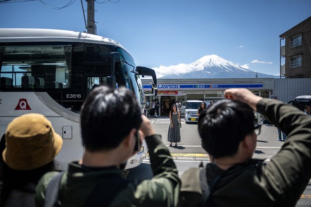 Tourists take pictures from the opposite street of a convenience store with Mount Fuji on May 3, 2024, before a huge black barrier which will be installed to block Mount Fuji from view, in the town of Fujikawaguchiko, Yamanashi prefecture. (Photo by Philip Fong/AFP Photo)