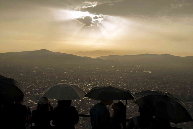 People hold umbrellas during a sudden rain shower in Lycabettus Hill , Athens, Greece, on Friday, May 17, 2024 as the sun sets through a haze of dust blown over from North Africa. Greek health officials have warned people with respiratory problems and other health issues to avoid outdoor exercise due to dust carried across the Mediterranean Sea from the Sahara Desert. The dust is expected to persist for several days, while temperatures are forecast to exceed 30 degrees Celsius (86 Fahrenheit) in parts of Greece Saturday. (Photo by Petros Giannakouris/AP Photo)