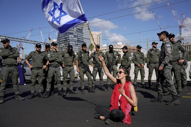 A demonstrator waves the Israeli flag seated on a highway while flanked by paramilitary border police during a protest against plans by Prime Minister Benjamin Netanyahu's government to overhaul the judicial system, in Tel Aviv, Israel, Thursday, March 9, 2023. (Photo by Ariel Schalit/AP Photo)