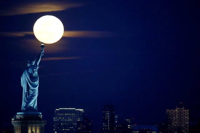 A full moon rises over the Statue of Liberty seen from the Port Liberte neighborhood of Jersey City, N.J., Monday, February 22, 2016. (Photo by Julio Cortez/AP Photo)