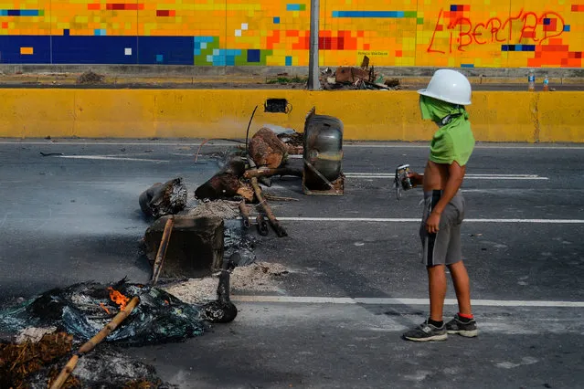 A young protester remains by a roadblock during a protest against Venezuelan President Nicolas Maduro in Caracas, on June 14, 2017. With Venezuelans suffering from high inflation, food shortages and soaring crime rates, plus a deepening corruption scandal, the Venezuelan opposition has mounted near- daily anti- government protests since April 1. The protests have left 68 dead so far and more than a thousand injured, according to prosecutors. (Photo by Luis Robayo/AFP Photo)