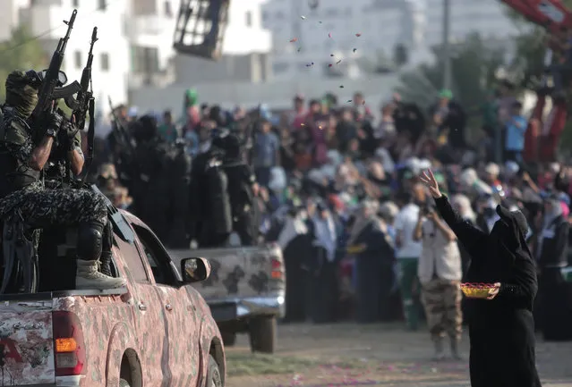 A Palestinian woman throws candy on Hamas masked gunmen with their guns during a graduation ceremony of the Hamas, Liberation Youth, military summer camp, in Gaza City, Wednesday, August 5, 2015. (Photo by Khalil HamraAP Photo)