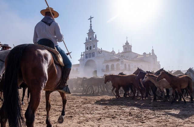 Some of the 1,500 semi-wild horses trot in front of the Chapel of El Rocio on their way to the pen during the traditional “Saca de las Yeguas” round-up in Almonte, Huelva, southern Spain on June 26, 2023. In a tradition held for more than 500 years, annually on 26 June several locals called “yeguerizos” from the town of Almonte search their herds, that have been grazing freely in several enclaves of Donana Natural Park, and move then to the town. (Photo by Julian Perez/EPA)