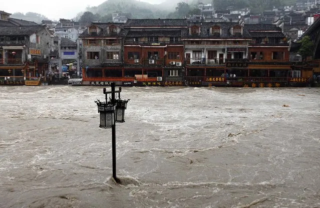 A street lamp is seen in floodwaters in front of partially submerged buildings by an overflowing river at the ancient town as heavy rainfall hits Fenghuang county, Hunan province July 15, 2014. More than 50,000 locals and tourists were evacuated since Monday night as record downpours hit Fenghuang county of central China's Hunan province, Xinhua News Agency reported. (Photo by Reuters/China Daily)