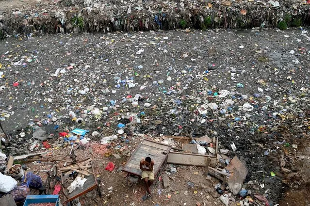 A man sits on a cart next to a sewer canal filled with plastics and other waste in New Delhi on June 30, 2022. (Photo by Money Sharma/AFP Photo)