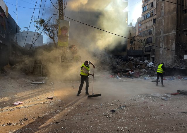 A worker cleans a street as smoke rises from a destroyed building that was hit by an Israeli airstrike in Dahiyeh, in the southern suburb of Beirut, Lebanon, early Sunday, October 20, 2024. (Photo by Hussein Malla/AP Photo)