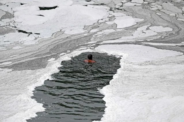 A scavenger looks for coins and recyclable materials amongst the religious offerings thrown by devotees in the waters of river Yamuna coated with polluted foam in New Delhi on July 5, 2022. (Photo by Sajjad Hussain/AFP Photo)