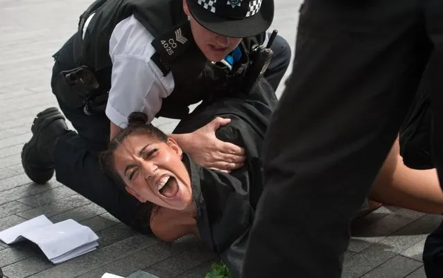 British policemen block a topless activist of Ukraine's prominent feminist rights group FEMEN as she was protesting near the Tower Bridge in Central London on August 2, 2012 on day 6 of the London 2012 Olympic games. FEMEN's activists organised an “islamic maraton” to demonstrate against “islamic regimes” they say being supported by the International Olympic Committee. (Photo by Will Oliver/AP Photo)