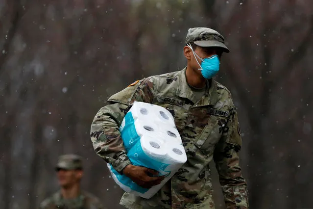 A member of Joint Task Force 2, composed of soldiers and airmen from the New York Army and Air National Guard, wears a face mask while carrying paper towels as he arrives to sanitize and disinfect the Young Israel of New Rochelle synagogue, as snow falls during the coronavirus disease (COVID-19) outbreak in New Rochelle, New York, U.S., March 23, 2020. (Photo by Andrew Kelly/Reuters)