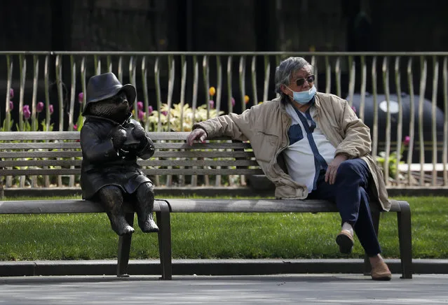 A man relaxes on a bench in London, next to a sculpture of Paddington Bear, as the country is in lockdown to help curb the spread of the coronavirus, Wednesday, April 15, 2020. The highly contagious COVID-19 coronavirus has impacted on nations around the globe, many imposing self isolation and exercising social distancing when people move from their homes. (Photo by Frank Augstein/AP Photo)