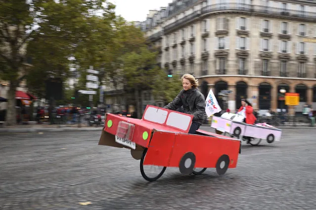 People ride a cardboard car on Place de la Bastille during a “car free” day in Paris on October 1, 2017. Parisians were encouraged to roller-blade, bike or stroll through the City of Light for a “car-free” day intended to leave the streets vacant for slower, clean forms of transport. October 1, marks the third time the French capital has experimented with a car ban, but it is by far the most ambitious with the zone set aside for pedestrians or cyclists covering the entire historic heart of the city – 105 square kilometres (40 square miles). (Photo by Eric Feferberg/AFP Photo)