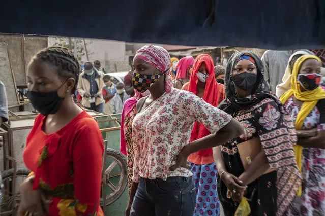 In this photo taken Saturday, April 25, 2020, Ndyeye Fatou, center, the daughter of Bara Tambedou, wears a patterned face mask as she queues to buy bread for her family on the first day of the Muslim fasting month of Ramadan, in Dakar, Senegal. This year the family is celebrating Ramadan at home, with prohibitions on public gatherings and a dusk-to-dawn curfew in place to curb the spread of the new coronavirus. (Photo by Sylvain Cherkaoui/AP Photo)