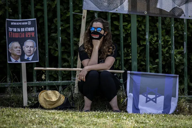 A woman wears a mask for protection against the spread of the coronavirus sits next to a sign that reads: “a government with 36 ministers? Where is the shame?” while they watching a live broadcast of an exceptionally large panel of 11 justices participated in the highly anticipated session in Israel's Supreme Court in Jerusalem, Sunday, May 3, 2020. Israel's high court heard petitions Sunday that seek to block Prime Minister Benjamin Netanyahu from forming a government because he has been charged with serious crimes. (Photo by Tsafrir Abayov/AP Photo)