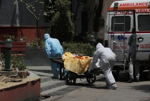 Health workers in personal protective suits ferry the body of a man who died of Covid 19 on a handcart for cremation in New Delhi, India, Thursday, May 28, 2020. India grappled with scorching temperatures and the worst locust invasion in decades as authorities prepared for the end of a months long lockdown despite recording thousands of new infections every day. (Photo by Manish Swarup/AP Photo)