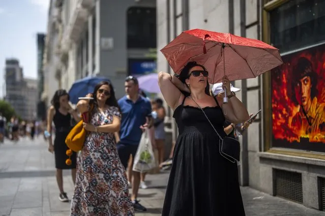A woman holds an umbrella to shelter from the sun during a hot sunny day in Madrid, Spain, Monday, July 18, 2022. (Photo by Manu Fernandez/AP Photo)