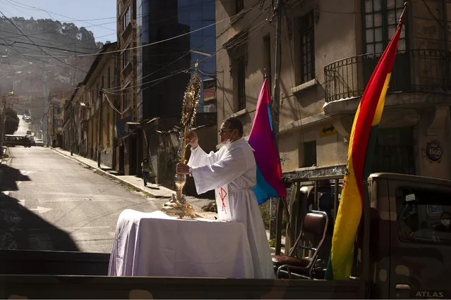 A Catholic priest rides in the back of a military vehicle as he holds on to a monstrance during a procession marking the Corpus Christi, which commemorates the biblical transubstantiation of bread and wine into the body and blood of Christ, in La Paz, Bolivia, Thursday, June 11, 2020. Due to the new coronavirus pandemic the religious holiday has been arranged to encourage faithful to stay home offering an online Mass and the procession to be escorted by members of the military. (Photo by Juan Karita/AP Photo)