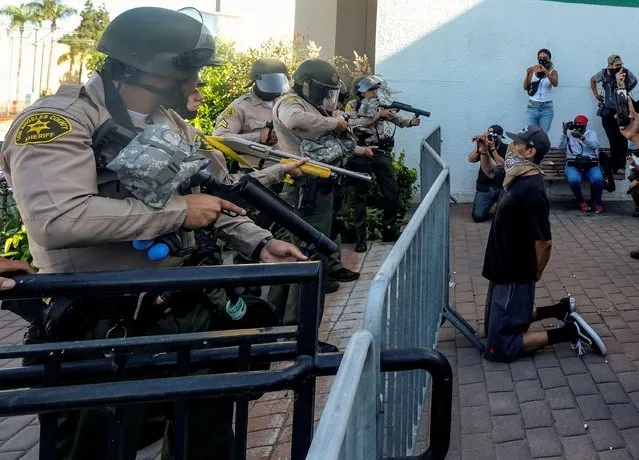 A demonstrator kneels as Los Angeles County sheriff's deputies prepare to fire pepper balls, flash-bangs and rubber bullets in a protest against the death of 18-year-old Andres Guardado and racial injustice, in Compton, California, June 21, 2020. (Photo by Ringo Chiu/Reuters)