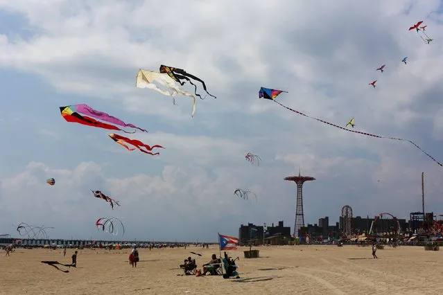 Kites fly in the sky as people sit and walk on the beach at Coney Island in the Brooklyn borough of New York, August 19, 2015. (Photo by Shannon Stapleton/Reuters)