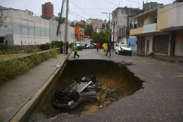 A car is seen in a hole on a road in Campestre La Laguna, Acapulco, Mexico after heavy rains caused flooding on September 4, 2016. A tropical depression with heavy rains lashing the country's Pacific coastal region has caused flooding and evacuation of families to temporary shelters. (Photo by Francisco Robles/AFP Photo)