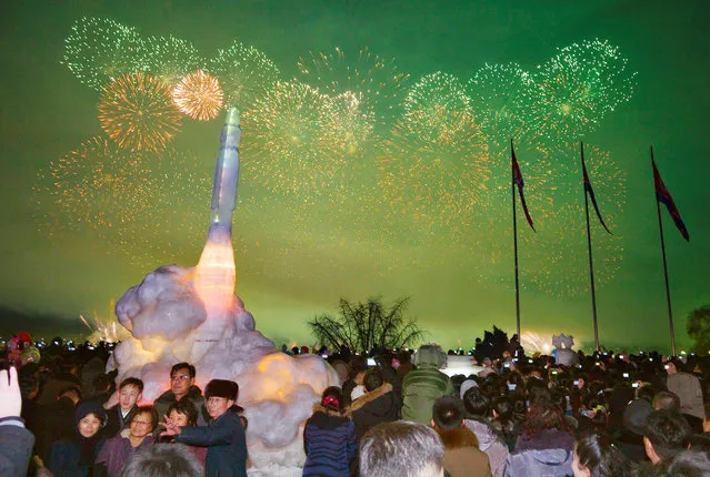 Fireworks are seen above the Taedong River during New Year celebrations as visitors pose for a photo in front of an ice sculpture of an intercontinental ballistic missile at the Pyongyang Ice Sculpture Festival in Kim Il Sung Square in Pyongyang, North Korea in this photo released by Kyodo January 1, 2018. (Photo by Reuters/Kyodo News)