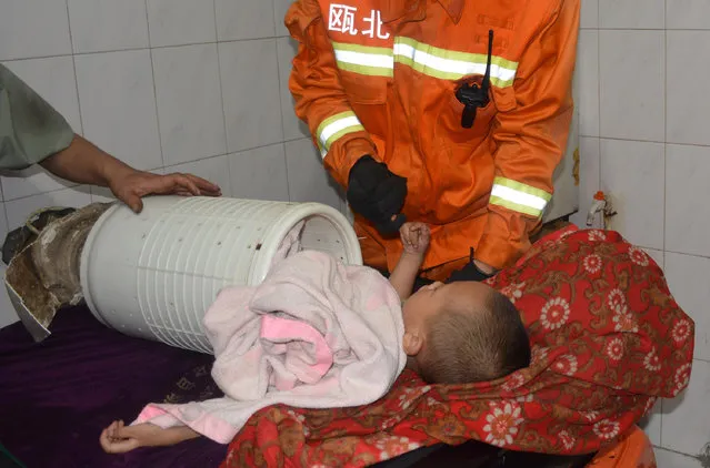 A three-year-old boy, stuck in the cylinder of a washing machine, hooks the pinky of a firefighter during a rescue operation in Yongjia county of Wenzhou, Zhejiang province, China July 10, 2014. Firefighters successfully rescued the boy, who got stuck while playing inside the washing machine, by tearing apart the machine and cutting the cylinder open, local media reported. The boy did not sustain any injuries, the report added. (Photo by Reuters/China Stringer Network)