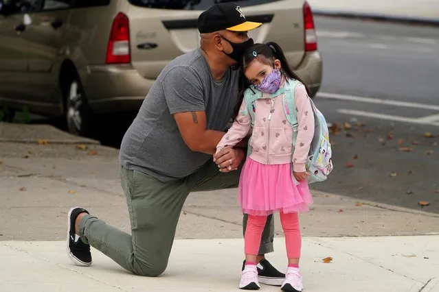 Joel Balcita comforts his daughter Sadie just before she attends her first day of grade 1 at P.S. 130 in the Brooklyn borough of New York City, New York, U.S., September 29, 2020. (Photo by Carlo Allegri/Reuters)