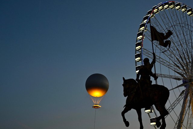 The reinstallation of the 2024 Olympic cauldron designed by French designer Mathieu Lehanneur lifts off at the Jardin des Tuileries, as a ferris wheel dominates the skyline, as seen from near the Monument a Jeanne d'Arc equestrian statue by French sculptor Emmanuel Fremiet, in Paris on June 21, 2025. (Photo by Christophe Delattre/AFP Photo)