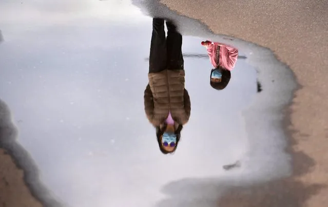 A mother and child wearing face masks are reflected in a puddle while walking in Melbourne's Docklands district on August 14, 2020 as the city battles an outbreak of the COVID-19 coronavirus. The state remains effectively sealed off from the rest of the country, with other regions so far largely spared from new infections. (Photo by William West/AFP Photo)