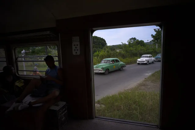 In this August 26, 2015 photo, antique American cars wait for an electric Hershey train to pass through the Casablanca municipality of Havana, Cuba. The train connects Casablanca to the city of Matanzas. In 1916 the Corporation of Pennsylvania Hershey built a network of electric railways to transport their products and workers to the Hershey sugar factory, just east of the capital. (Photo by Ramon Espinosa/AP Photo)