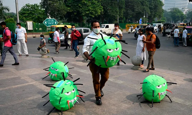An officer from the district magistrate office holds a Covid-19 coronavirus-themed mascot in a market area during an awareness campaign against coronavirus and rising air pollution levels in New Delhi on October 26, 2020. (Photo by Sajjad Hussain/AFP Photo)