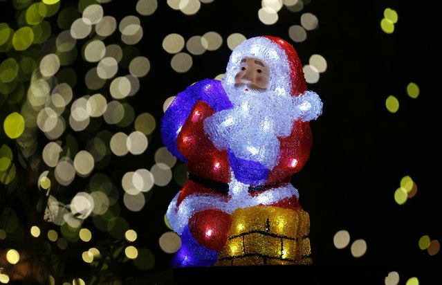 A Santa Claus figure sits on the chimney of a toy house in front of an illuminated house in the town of Stolberg near the western German city of Aachen December 16, 2014. (Photo by Wolfgang Rattay/Reuters)