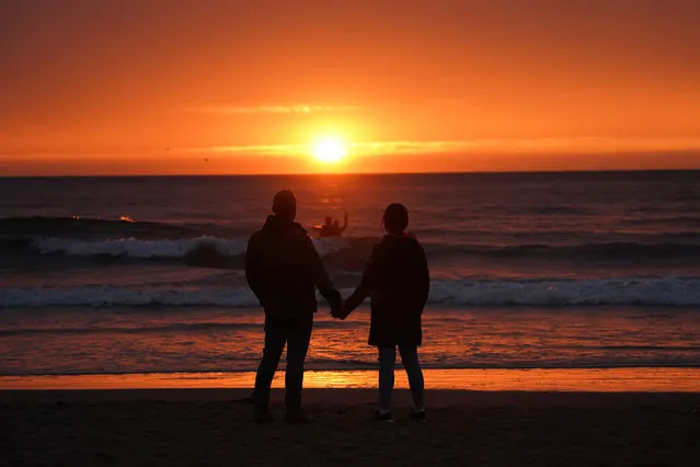 People watch the sunrise at Tynemouth after the shortest night following the summer solstice on June 21, 2020. The UK should cut greenhouse gas emissions by nearly four-fifths by 2035, climate advisers have said, signalling major changes to home heating. (Photo by Owen Humphreys/PA Images via Getty Images)