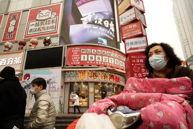 Residents wearing masks past by a screen showing a trailer for the film “Days and Nights in Wuhan” outside a mall in Wuhan in central China's Hubei province on Friday, January 22, 2021. China is rolling out the state-backed film praising Wuhan ahead of the anniversary of the 76-day lockdown in the central Chinese city where the coronavirus was first detected. (Photo by Ng Han Guan/AP Photo)