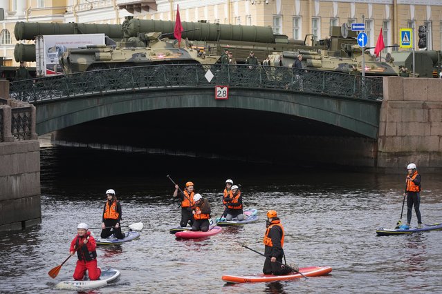 People steer their stand-up paddle boards along Moyka River past military vehicles prepared for a rehearsal for the Victory Day military parade which will take place at Dvortsovaya (Palace) Square on May 9 to celebrate 78 years after the victory in World War II in St. Petersburg, Russia, Sunday, May 7, 2023. (Photo by Dmitri Lovetsky/AP Photo)