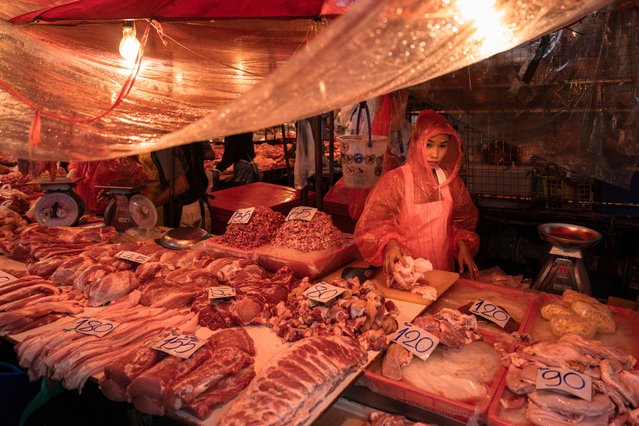 A woman selling fresh meat wears a raincoat at Khlong Toei Market during a rain storm in Bangkok, Thailand on May 14, 2025. (Photo by Chanakarn Laosarakham/AFP Photo)
