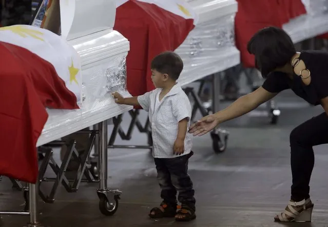 Christine Kiangan, widow of Noble Kiangan, one of the 44 members of the elite police commandos killed last Sunday during the Philippines' biggest single-day combat loss in recent years, reaches out to her son as he touches a commando's flag-draped coffin at Camp Bagong Diwa, Taguig city, south of Manila, Philippines, on Friday, January 30, 2015. (Photo by Bullit Marquez/AP Photo)
