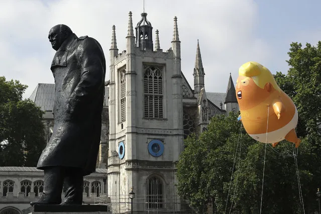 A six-meter high cartoon baby blimp of U.S. President Donald Trump hovers next to the statue of former British Prime Minister Winston Churchill, as it is flown as a protest against his visit, in Parliament Square in London, England, Friday, July 13, 2018. (Photo by Matt Dunham/AP Photo)