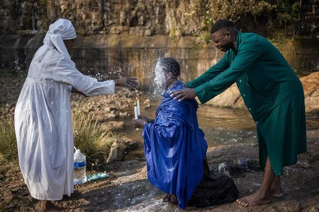 A woman pours milk over the head of another devotee during a cleansing ritual in a park in Johannesburg on September 10, 2023. With many South Africans being part of churches that reserve a central role to baptism and cleansing, every Sunday morning Johannesburg's rivers and water streams bustle with devotees and church members. (Photo by Michele Spatari/AFP Photo)