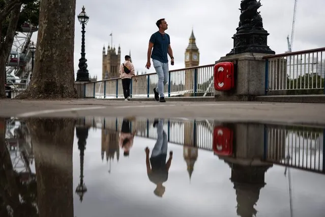 A pedestrian walks on the Southbank by the river Thames, in central London, on July 27, 2023 as he is reflected in a puddle with Elizabeth Tower, commonly called Big Ben, on a gloomy summer day. (Photo by Henry Nicholls/AFP Photo)
