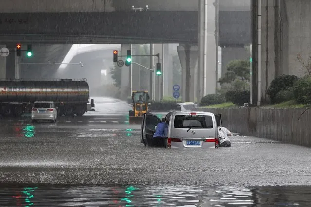 This photo taken on July 20, 2021 shows people pushing a van through flood waters along a street following heavy rains in Zhengzhou in China's central Henan province. (Photo by AFP Photo/China Stringer Network)