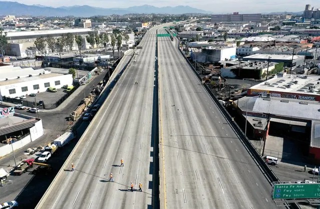 An aerial view of workers walking on the closed I-10 freeway following a large pallet fire (CENTER R), which occurred Saturday at a storage yard, on November 13, 2023 in Los Angeles, California. Engineers have been assessing the extent of the damage and it remains unknown how long the freeway, which is a major commuter artery through the downtown area, will remain closed and complicate traffic for the city. California Gov. Gavin Newsom said that over 300,000 vehicles drive through the freeway corridor each day and drivers are being urged to use public transit. (Photo by Mario Tama/Getty Images)