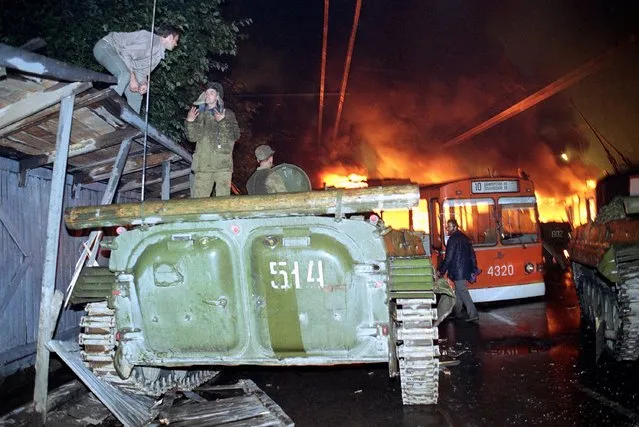 In this Wednesday morning, August 21, 1991 file photo, a trolley bus that was used by anti-coup demonstrators to block the exit of Soviet armored personnel carriers from the area near the Soviet Foreign Ministry office burns during a verbal confrontation between demonstrators and Soviet soldiers standing atop an armored vehicle in downtown Moscow, Russia. (Photo by Alexander Zemlianichenko/AP Photo/File)