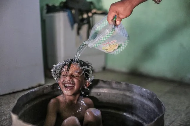 A Palestinian mother washes her son in their house during hot weather in a slum on the outskirts of Khan Younis refugee camp, Gaza Strip, ​04 August 2021. (Photo by Mohammed Saber/EPA/EFE)