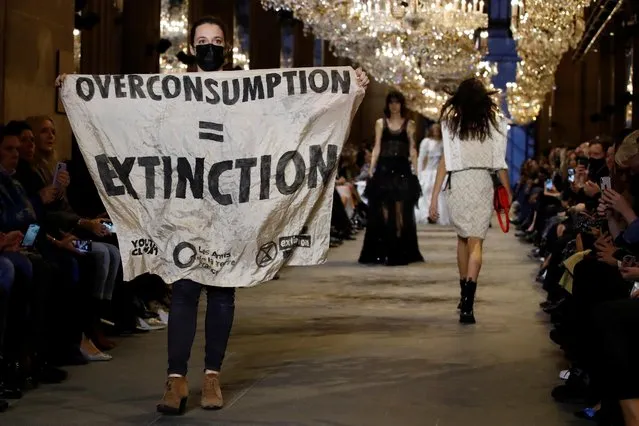 An activist walks on the ramp with a banner that says "Overconsumption = Extinction" as she crashes the designer Nicolas Ghesquiere Spring/Summer 2022 women's ready-to-wear collection show for fashion house Louis Vuitton during Paris Fashion Week in Paris, France, October 5, 2021. (Photo by Gonzalo Fuentes/Reuters)