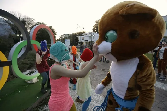 p*ssy Riot member Nadezhda Tolokonnikova in the aqua balaclava, left, interacts with an Olympic mascot while the group perform next to the Olympic rings in Sochi, Russia, on Wednesday, February 19, 2014. Cossack militia attacked the punk group with horsewhips earlier in the day as the artists – who have feuded with Vladmir Putin's government for years – tried to perform under a sign advertising the Sochi Olympics. (Photo by David Goldman/AP Photo)