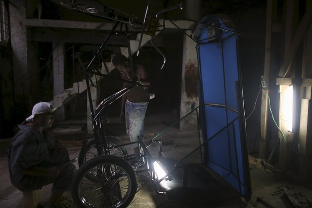 Alexander Ruval 43, (L) and Adrian Hernandez, 25, fix a pedicab in downtown Havana, March 21, 2016. (Photo by Alexandre Meneghini/Reuters)