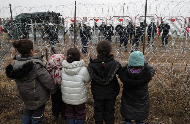 Children stand in front of a fence and address Polish law enforcement officers, who stand on the other side of the frontier, on the Belarusian-Polish border in the Grodno region, Belarus November 17, 2021. (Photo by Maxim Guchek/BelTA/Handout via Reuters)