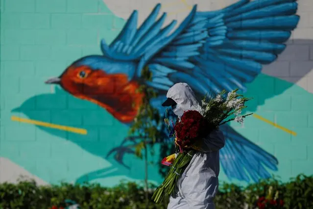 A cemetery worker looks to put flowers on the grave of a person who died of the coronavirus disease (COVID-19), during the Day of the Dead celebration, at La Bermeja cemetery in San Salvador, El Salvador on November 2, 2021. (Photo by Jose Cabezas/Reuters)